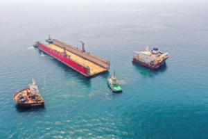 Semi-submersible heavy transport vessel Seaway Hawk at sea with tugboats maneuvering a large floating dock
